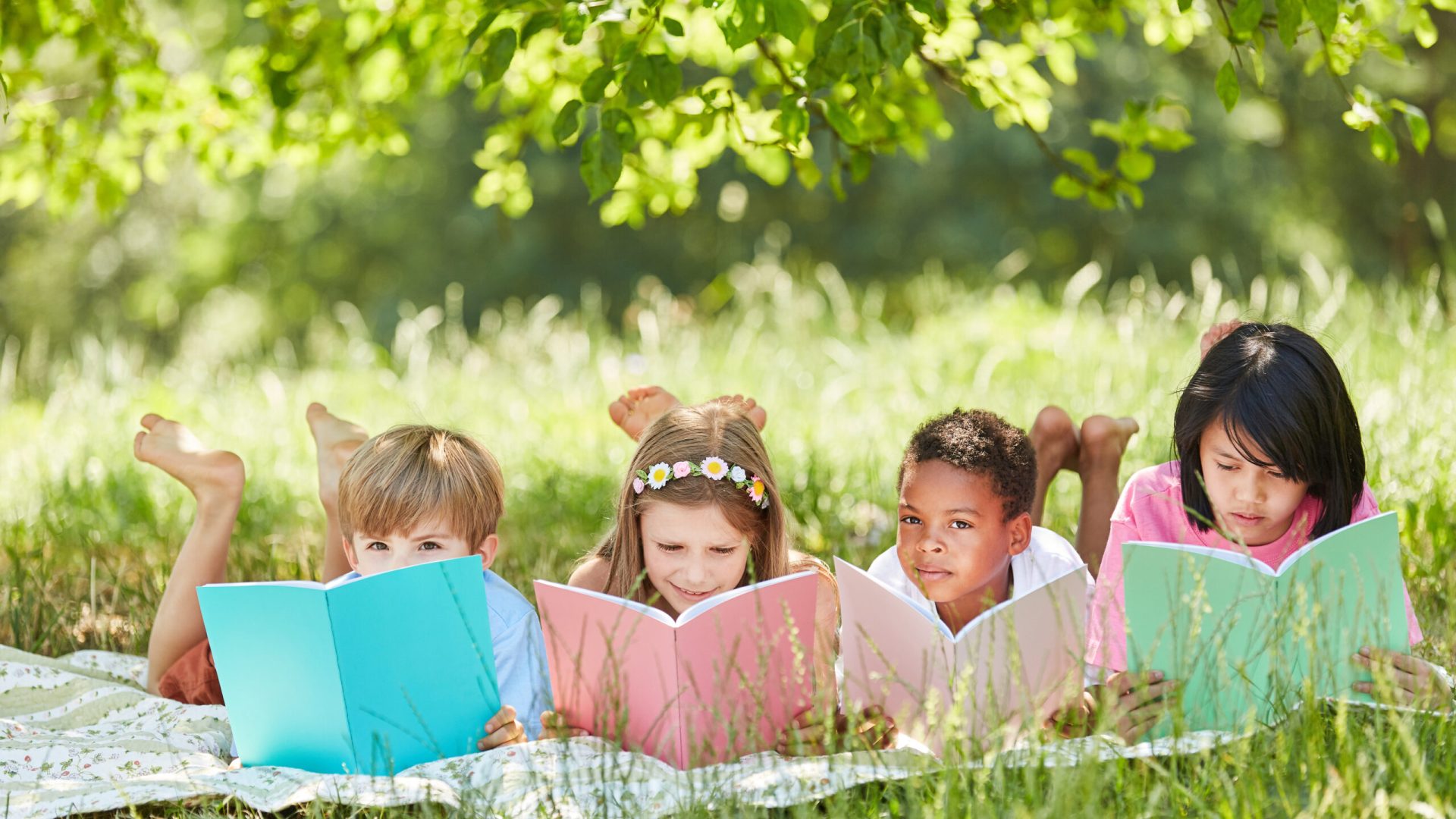 Multicultural,Group,Of,Children,Reading,While,Studying,In,The,Park